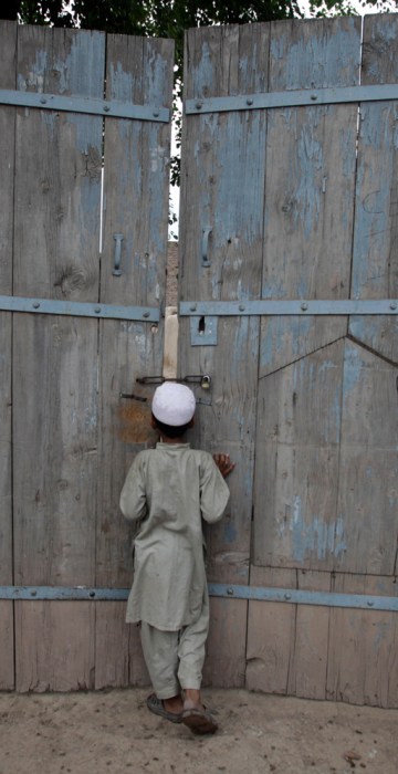 Image: A boy looks through the gate of the ancestral home of Shahzad in  Pakistan