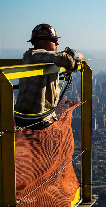Image: An iron worker looks at the New York skyline after watching a crane lift the final piece of the spire to the top of the One World Trade Center in New York