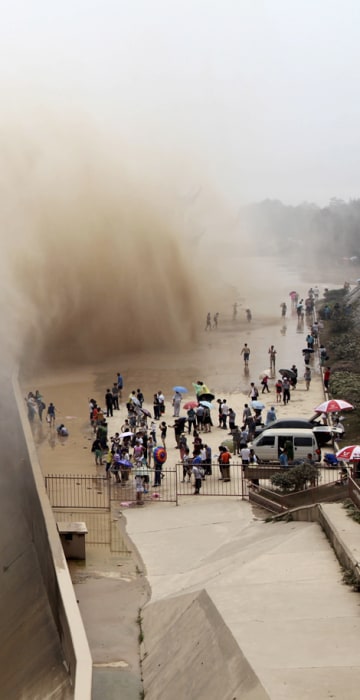 Image: Visitors watch water gushing from the section of the Xiaolangdi Reservoir on the Yellow River, during a sand-washing operation in Jiyuan