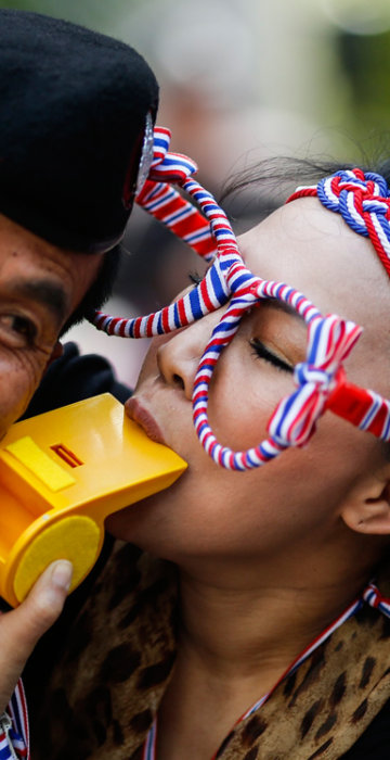 Image: An anti-government protester blows on a whistle next to a riot policeman as she gathers with others outside the headquarters of the ruling Puea Thai Party of Prime Minister Yingluck Shinawatra in Bangkok