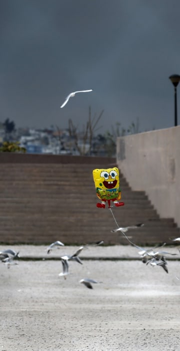 Image: A migrant boy runs while holding a balloon outside the Tae Kwon Do stadium at the southern suburb of Faliro in Athens