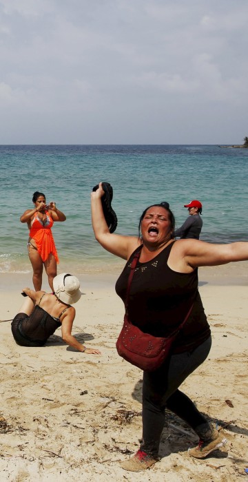 Image: A Cuban migrant shouts \"Cuba\" after arriving to the beach after crossing the border from Colombia through the jungle as tourist stand by in La Miel, in the province of Guna Yala, Panama