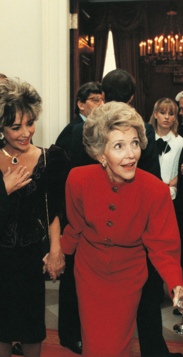 Nancy Reagan tugs on Ronald's coat as he talks with Tom Selleck with Elizabeth Taylor in tow on Jan. 20, 1985.