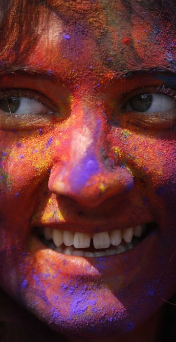 Image: A woman with coloured powder smeared on her face smiles as she celebrates Holi, the Festival of Colours, in Kathmandu