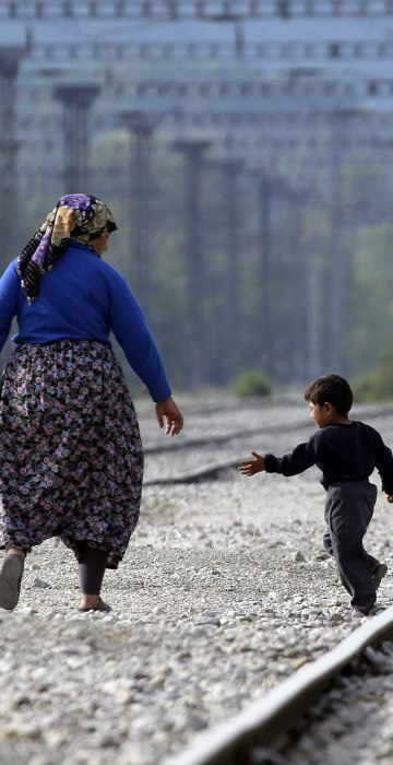 Image: A woman walks with a child along the train tracks near a makeshift camp at the northern Greek border point of Idomeni