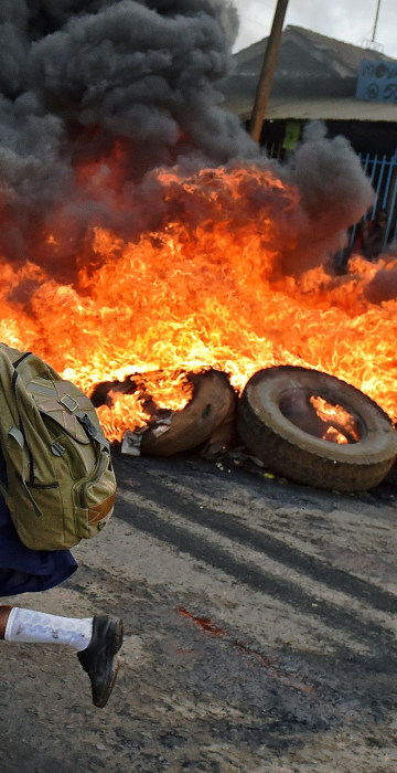 Image: A schoolgirl runs past a burning barricade in Kibera slum