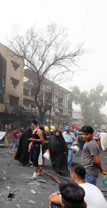 Image: Iraqis, including firefighters, gather at the site of a suicide car bombing