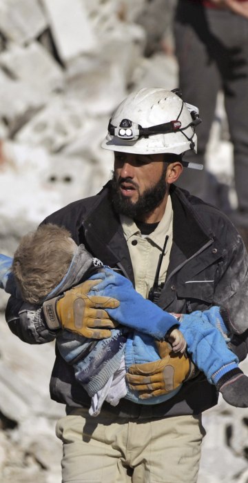 Image: A civil defence member carries a dead child in a site hit by what activists said were airstrikes carried out by the Russian air force in the rebel-controlled area of Maaret al-Numan town in Idlib province, Syria