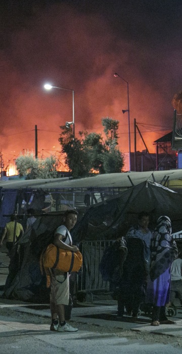 Image: Migrants hold their belonging as a large fire burns inside the Moria refugee camp