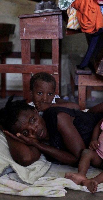Image: A woman with two of her children rest on the floor at the shelter set up in the Lycee Philippe Guerrier ahead of Hurricane Matthew in Les Cayes
