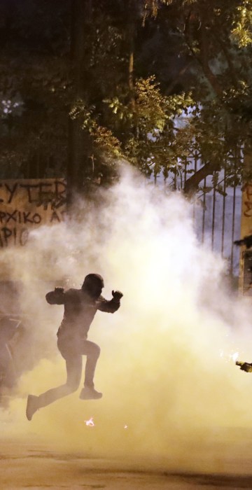 Image: A protester jumps to avoid tear gas as another one prepares to throw a firebomb during a protest against the visit of US President Barack Obama