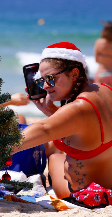 Image: Irish backpacker Genna Woods adjusts her small Christmas tree she planted in the sand as she celebrates Christmas Day at Sydney's Bondi Beach in Australia