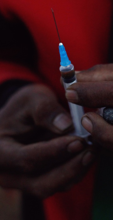 Image: A miner holds in his hands a jade stone and a syringe to use heroin at a mine dump at a Hpakant jade mine in Kachin state