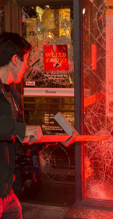 Image: A man pulls a piece of metal out of a window as a flare burns inside a Wells Fargo Bank
