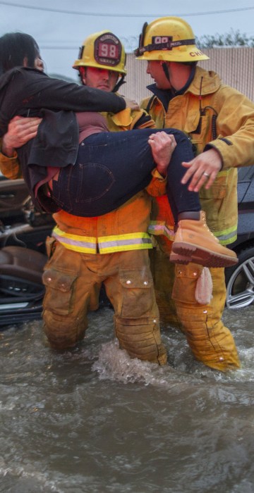 Image: A firefighter carries a woman from her car after it was caught in street flooding