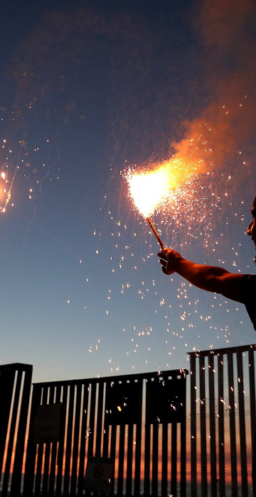 Image: A man shoots off fireworks next to the US-Mexican border fence.