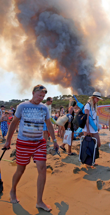 Image: Tourists evacuate the beach as smoke fills the sky above a burning hillside in Bormes-les-Mimosas