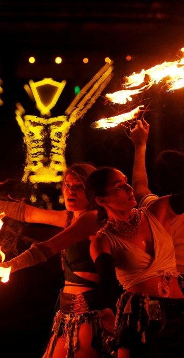 Image: Burning Man participants from the \"Revolutionary Motion\" fire conclave spin fire in front of the effigy of \"The Man\" just before the effigy is burned at the culmination of the annual Burning Man arts and music festival in the Black Rock desert of N