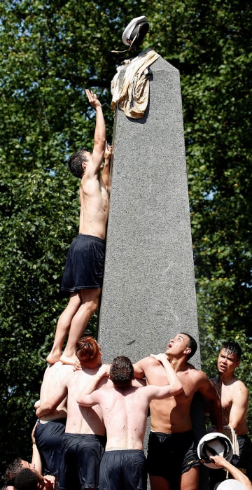 Image: A plebe places a midshipman's cap on top of the grease covered 21-foot Herndon Monument