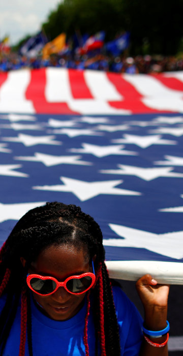 Image: A girl carries a U.S. flag as she takes part in a parade during Fourth of July Independence Day celebrations in Washington, D.C.