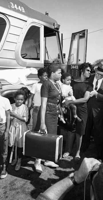 Victoria Bell, wearing glasses, holding infant, is greeted by Selectman E. Thomas Murphy on arrival from Little Rock., Ark