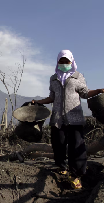 Image: Mount Merapi volcano spews ash as a villager collects her valuables from the ruins of her house at Kali Tengah village in Sleman