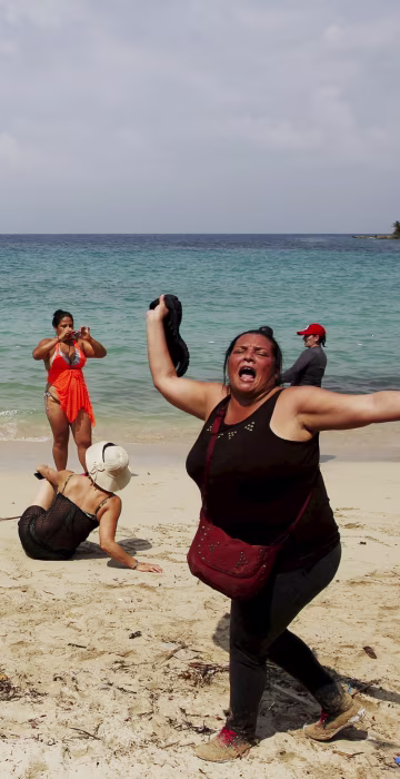 Image: A Cuban migrant shouts \"Cuba\" after arriving to the beach after crossing the border from Colombia through the jungle as tourist stand by in La Miel, in the province of Guna Yala, Panama