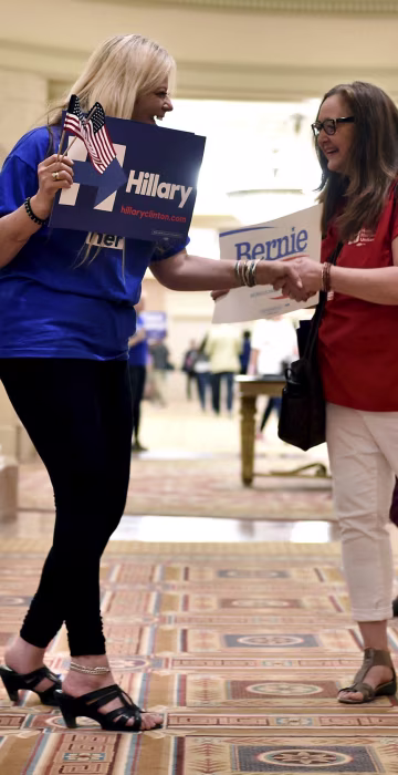 Image: People shake hands holding placards in support of their respective Democratic candidate
