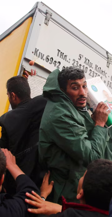 Image: Migrants try to get products from a truck at a makeshift camp on the Greek-Macedonian border near the village of Idomeni