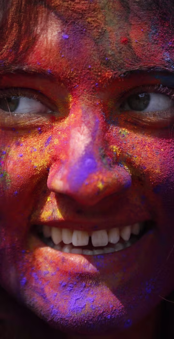 Image: A woman with coloured powder smeared on her face smiles as she celebrates Holi, the Festival of Colours, in Kathmandu