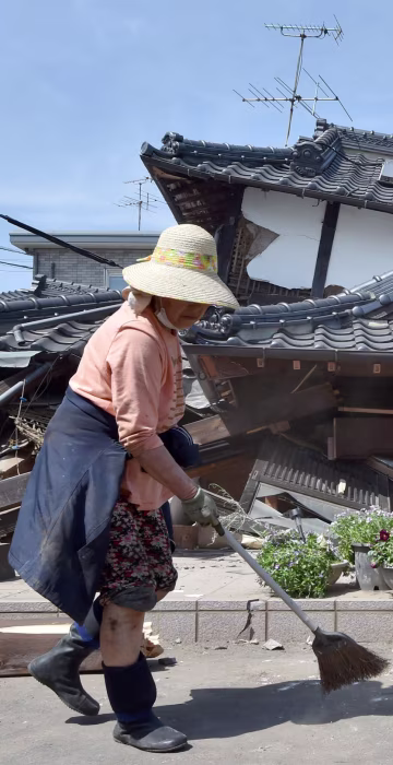 Image: A woman cleans up in front of her collapsed house