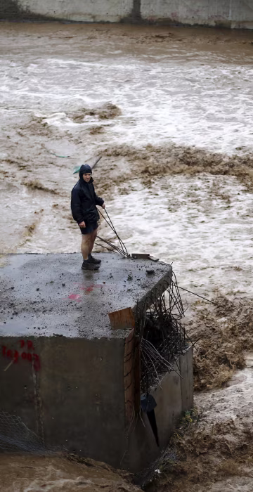 Image: A man is seen next to a river during floods in Santiago