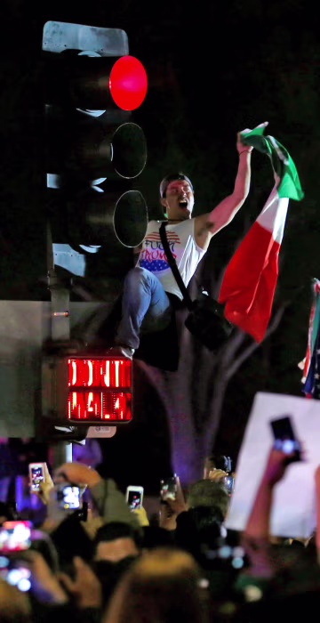 Image: A demonstrator climbs a traffic light outside Republican U.S. presidential candidate Donald Trump's campaign rally in Costa Mesa