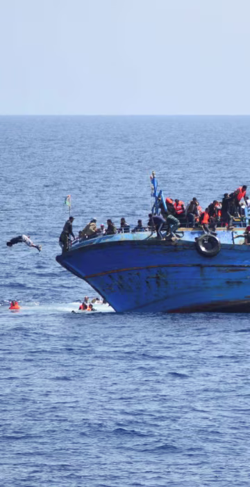 Image: Migrants are seen on a capsizing boat before a rescue operation by Italian navy ships \"Bettica\" and \"Bergamini\" (unseen) off the coast of Libya