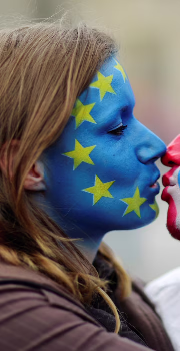 Image: Two activists with the EU flag and Union Jack painted on their faces kiss each other in front of Brandenburg Gate to protest against Brexit in Berlin