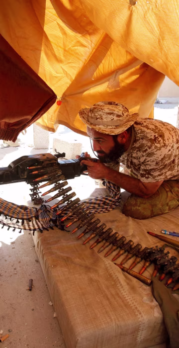 Image: Fighter from Libyan forces allied with the U.N.-backed government aims his weapon as he takes a position on a building rooftop during a battle with Islamic State militants in Sirte