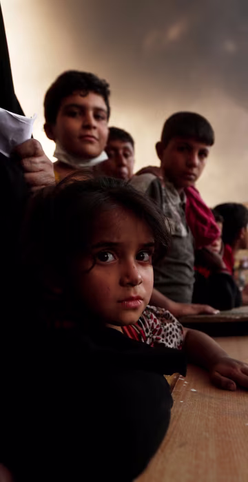 Image: Newly displaced people wait to receive food supplies at a processing center for displaced people In Qayyara