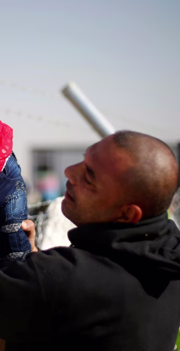 Image: A displaced Iraqi man, who fled the Islamic State stronghold of Mosul, holds his daughter to be seen by her grandmother through a fence at Khazer camp