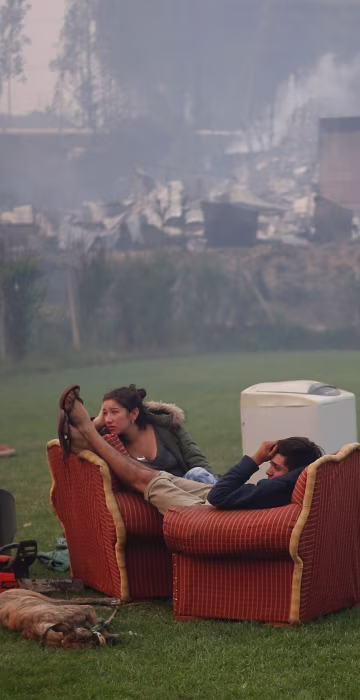 Image: A young couple rest in a football field after a forest fire devastated Santa Olga