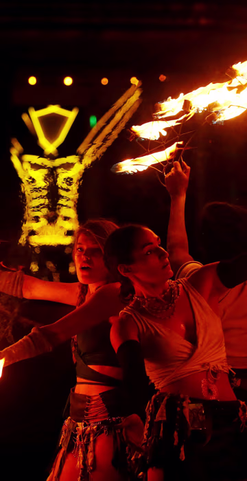 Image: Burning Man participants from the \"Revolutionary Motion\" fire conclave spin fire in front of the effigy of \"The Man\" just before the effigy is burned at the culmination of the annual Burning Man arts and music festival in the Black Rock desert of N