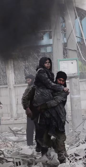 Image: A Syrian man carries an injured woman following air strikes