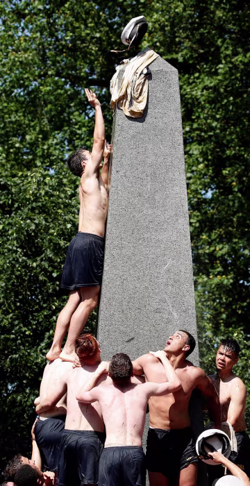Image: A plebe places a midshipman's cap on top of the grease covered 21-foot Herndon Monument