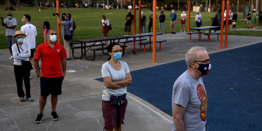 Image: Voters wearing protective masks stand in a socially distanced line to cast ballots at a voting polling location.