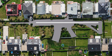 Photo illustration: An aerial view of a suburban neighborhood with an assault rifle shaped road in the middle.