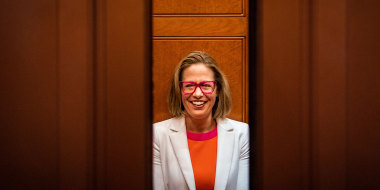 Image: Sen. Kyrsten Sinema (D-AZ) smiling while talking to reporters as the elevator door closes.