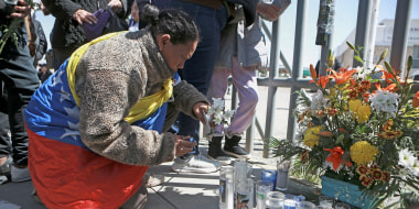 A woman places flowers in front of a gate that has been converted into a memorial outside a Mexican immigration detention center 