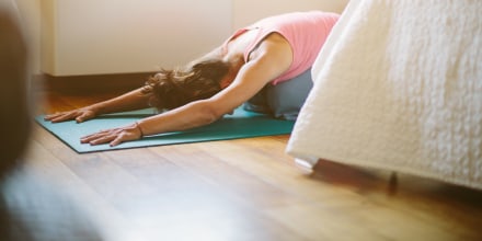 image: Mid adult woman in yoga position on bedroom floor