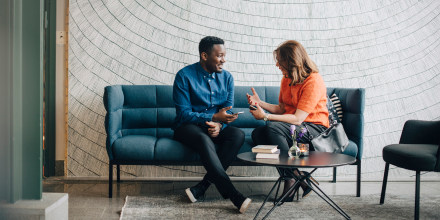 Image: Businessman and woman taking while sitting on couch against wall at conference