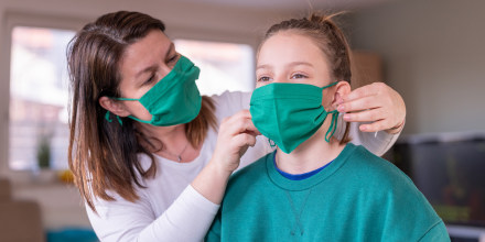 Mother wearing a homemade protective mask and putting one to her daughter