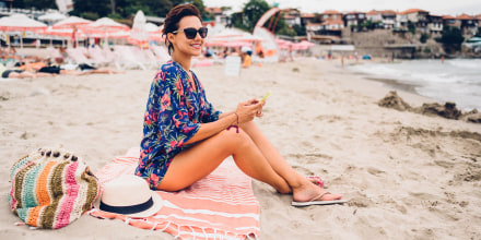 Image of a Woman sitting on the beach sitting on her pink striped beach towel